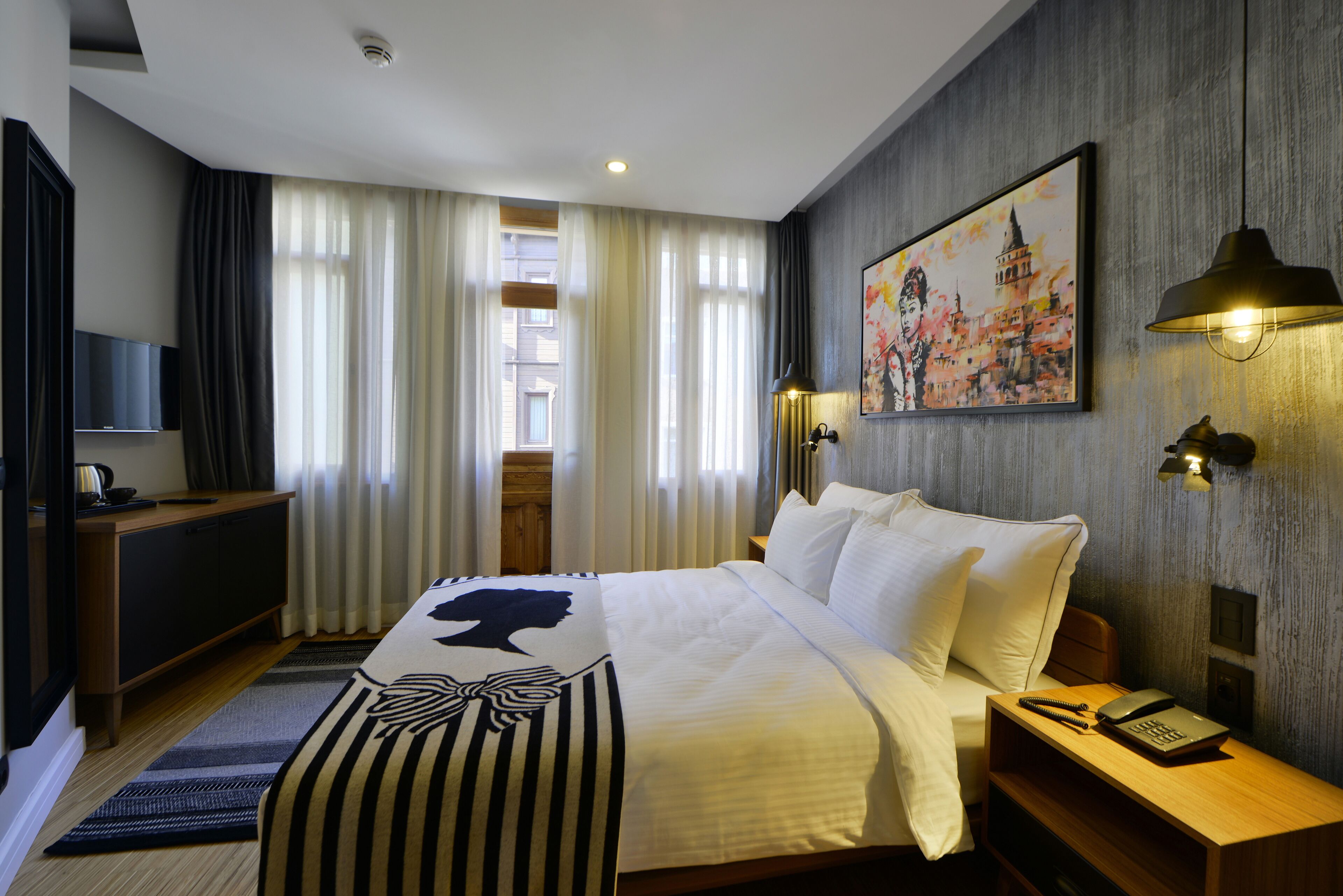 A hotel room with a bed, bedside table, lamp, painting, and a TV on a stand.