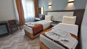 Une chambre d’hôtel avec deux lits, un bureau, une chaise et une grande fenêtre avec des rideaux.