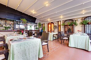 A restaurant with multiple tables, wicker chairs, and potted plants. - Arena Hotel - Special Class (Istanbul)