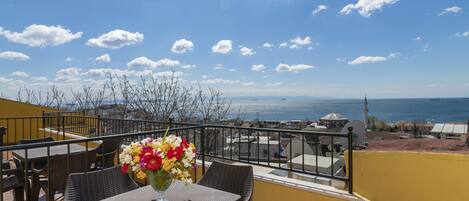 Una terraza con mesa y sillas, un florero y vistas al mar y edificios.
