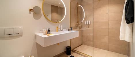 Un baño moderno con tocador blanco, cabina de ducha de vidrio y espejo con marco dorado.