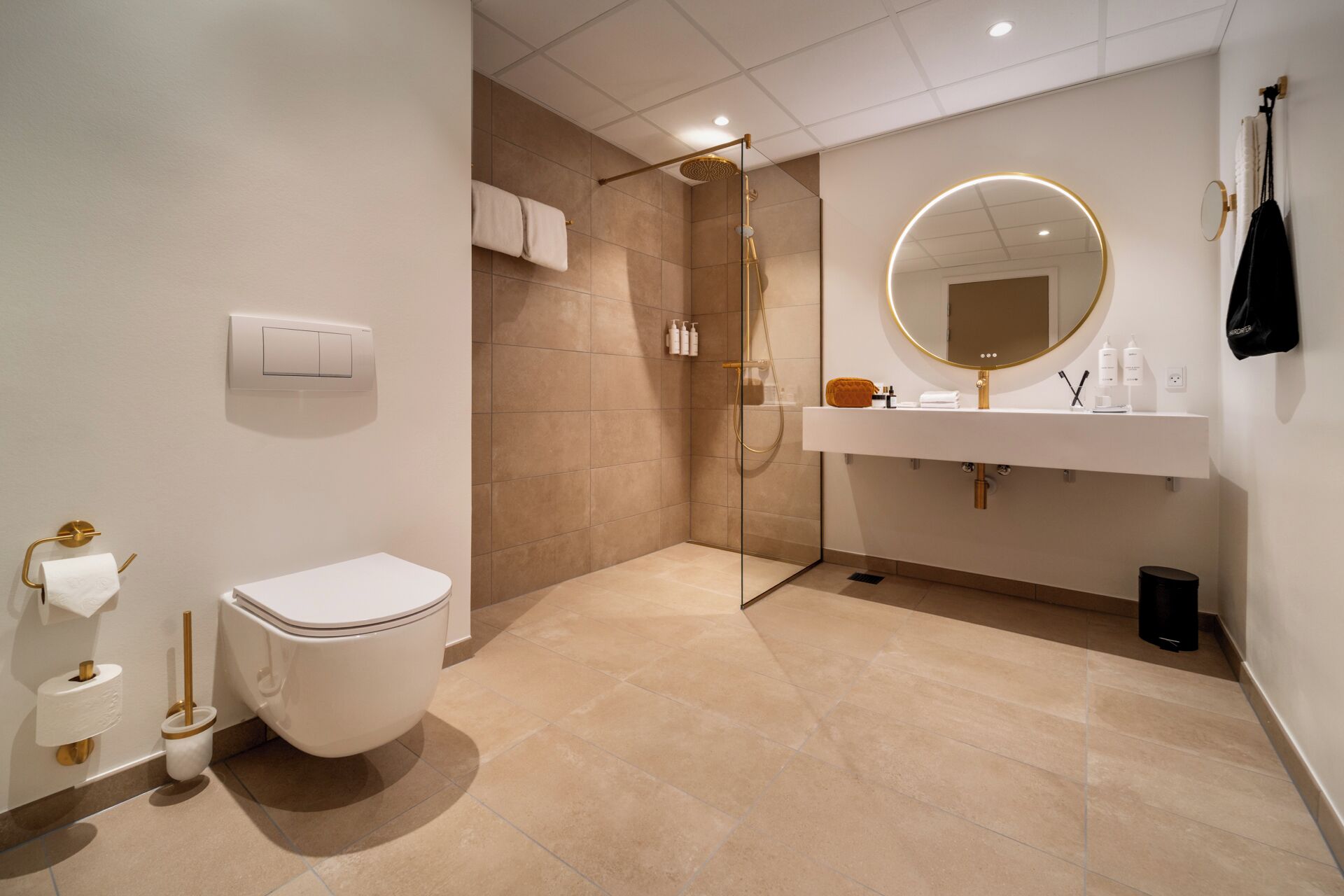 Un baño moderno con inodoro, ducha envuelta en vidrio, tocador con espejo y un perchero para toallas.