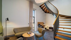 Una sala de estar moderna con un sofá, sillones, una mesita, un escritorio con una silla y una escalera espiral de madera.
