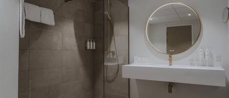 Ein modernes Badezimmer mit einer gläsernen Duschkabine, einem weißen Waschbecken mit goldfarbener Spiegel und Pflegeprodukten auf der Ablagefläche.