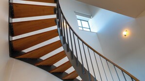 Una escalera de madera con barandas de metal y un pequeño ventanal con una lámpara.