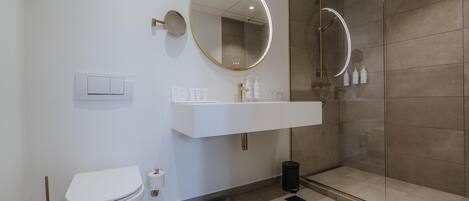Un baño moderno con inodoro, lavabo con espejo y cabina de ducha con mampara de vidrio.