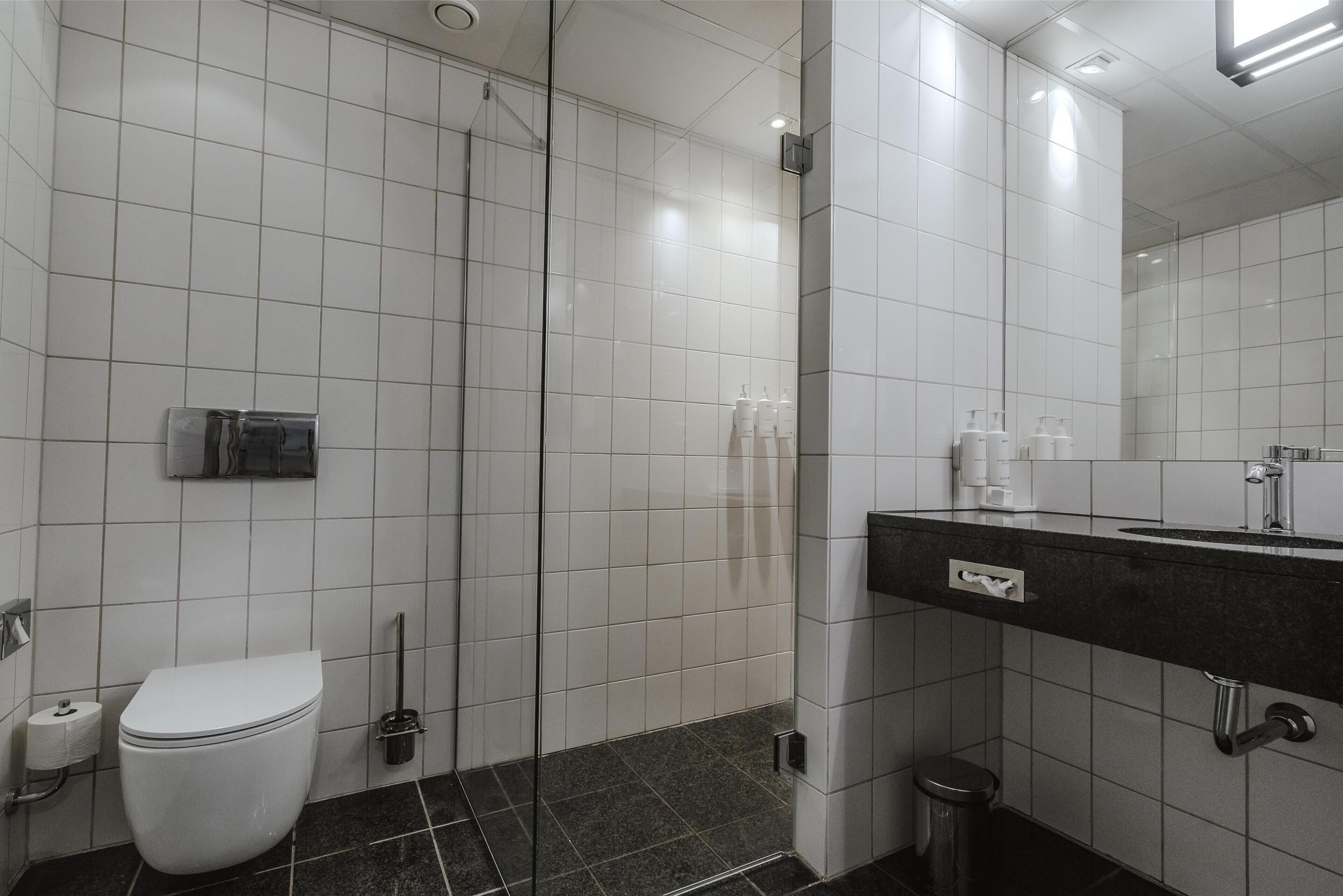 A modern bathroom with white tiles, a black marble floor, a white toilet, a glass-enclosed shower, and a black countertop with a mirror.