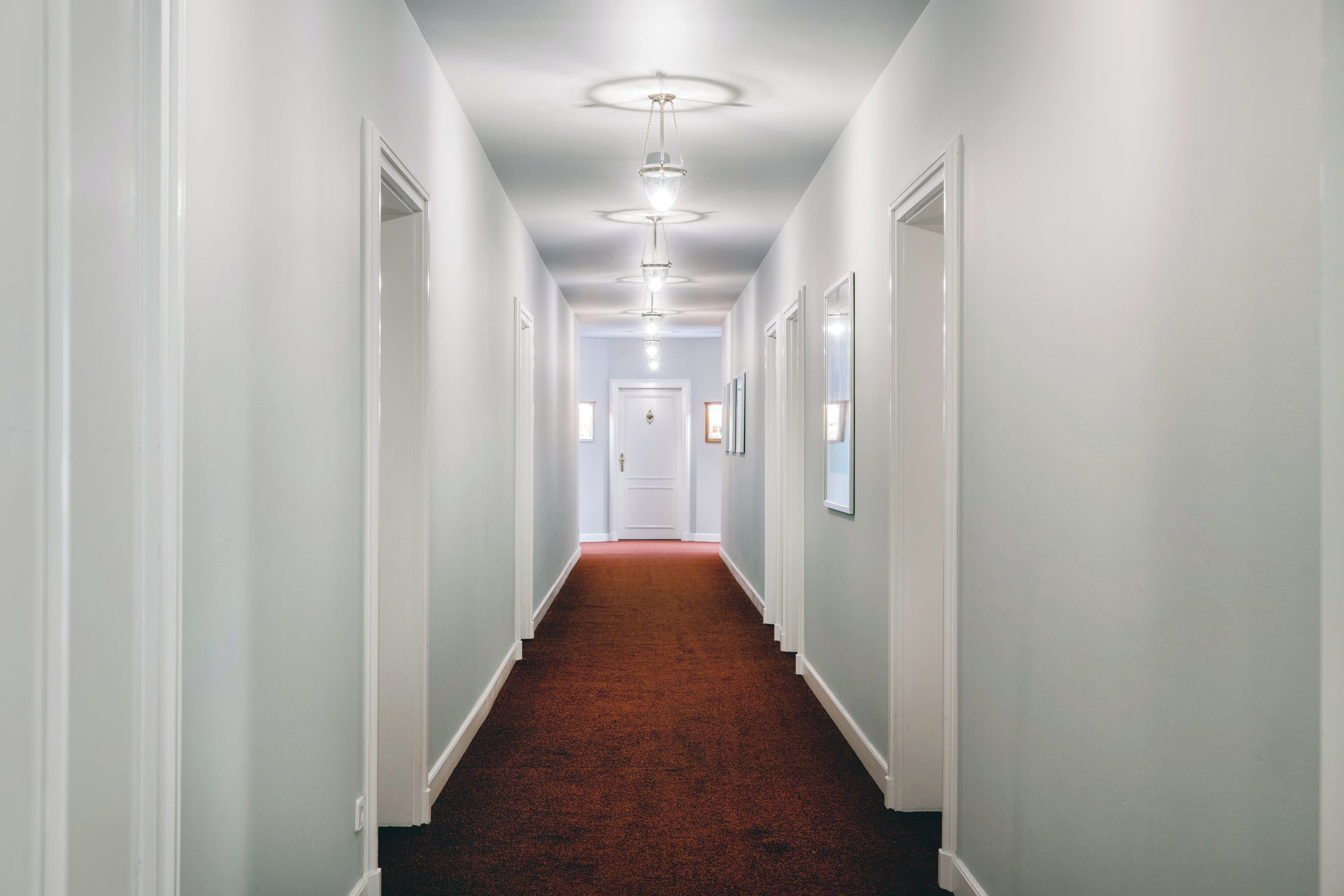 A long, narrow hallway with white walls and a red carpet.