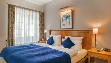 A hotel room with a large bed, two bedside tables, a nightstand, a lamp, and a framed picture on the wall.