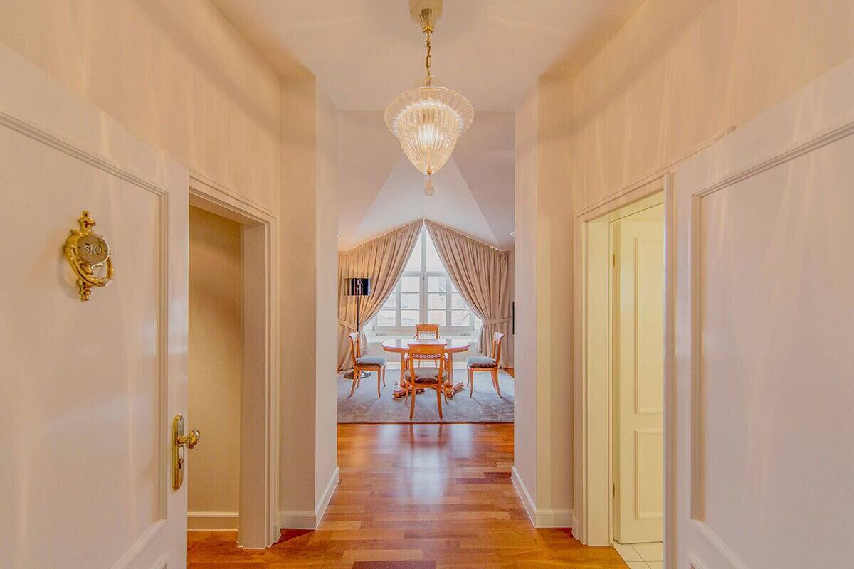 A hallway with a chandelier, a dining area with a table and chairs, and a window with curtains.