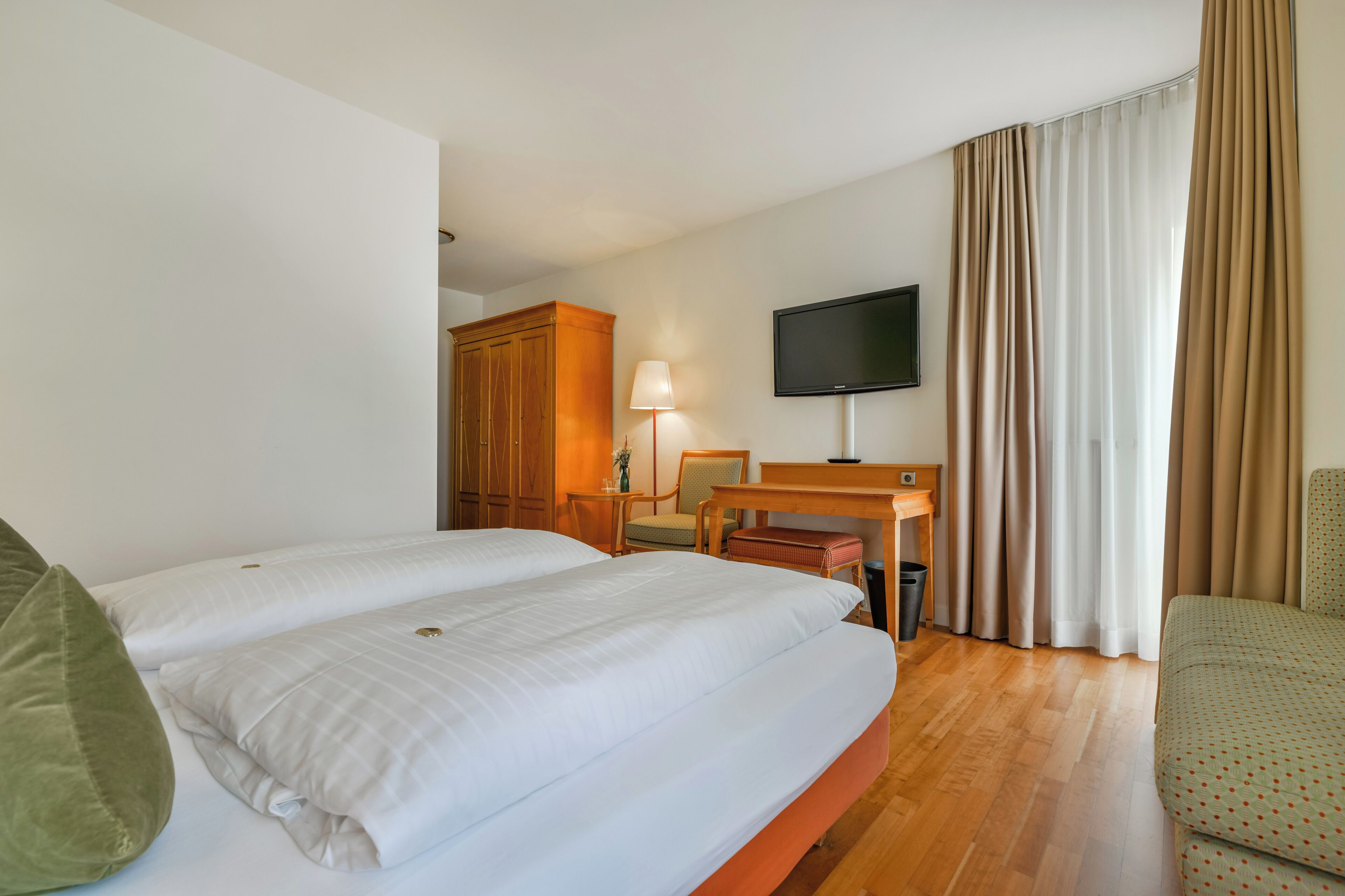 A hotel room with two beds, a desk, a chair, a TV, and a wardrobe.