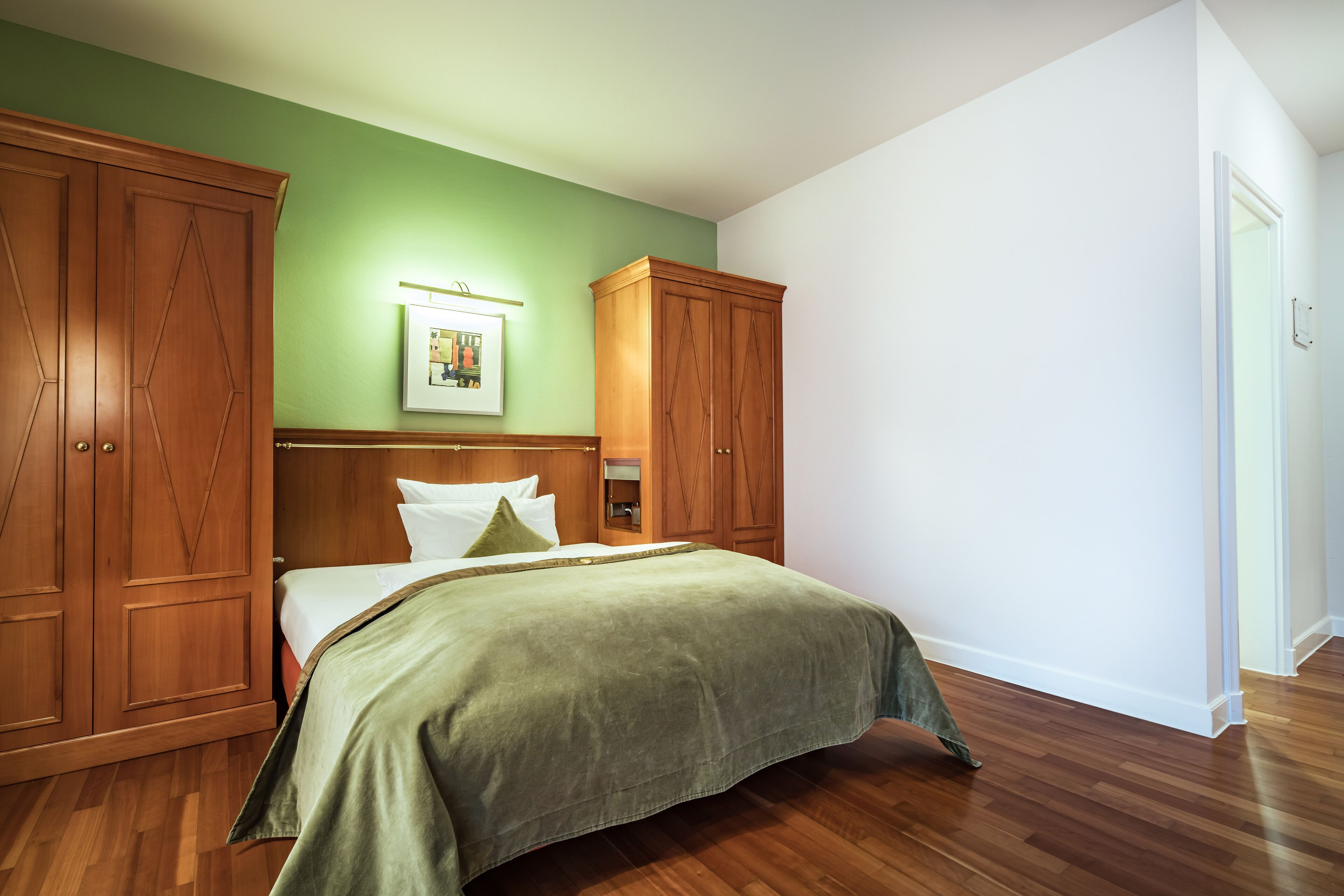 A bedroom with a bed, wooden wardrobe, and a green wall.