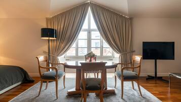 A corner room with a dining table, four chairs, a TV, and a window with curtains.