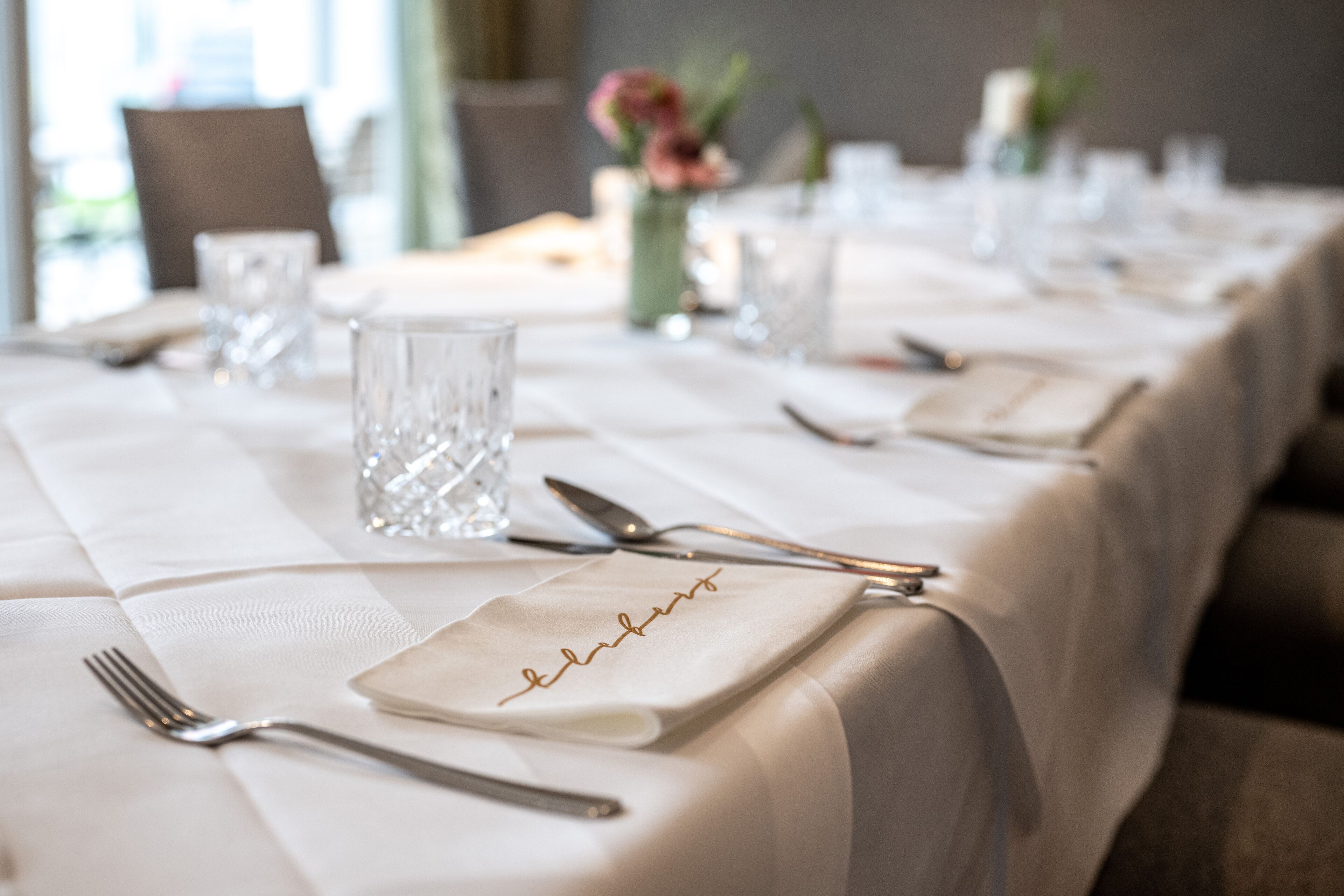 A neatly set dining table with a white tablecloth, clear glassware, and cutlery.