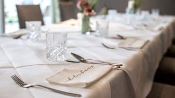 A neatly set dining table with a white tablecloth, clear glassware, and cutlery.