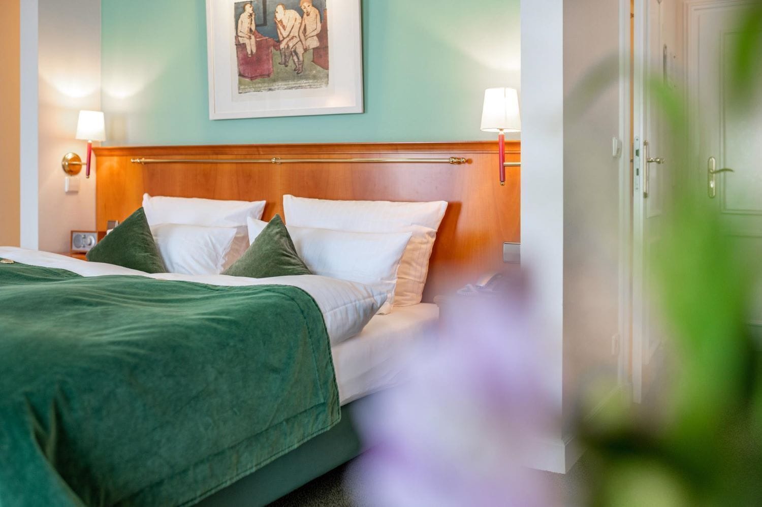Ein Hotelzimmer mit Bett, Kissen, Kopfteil, Nachttischlampen und einem gerahmten Bild an der Wand.