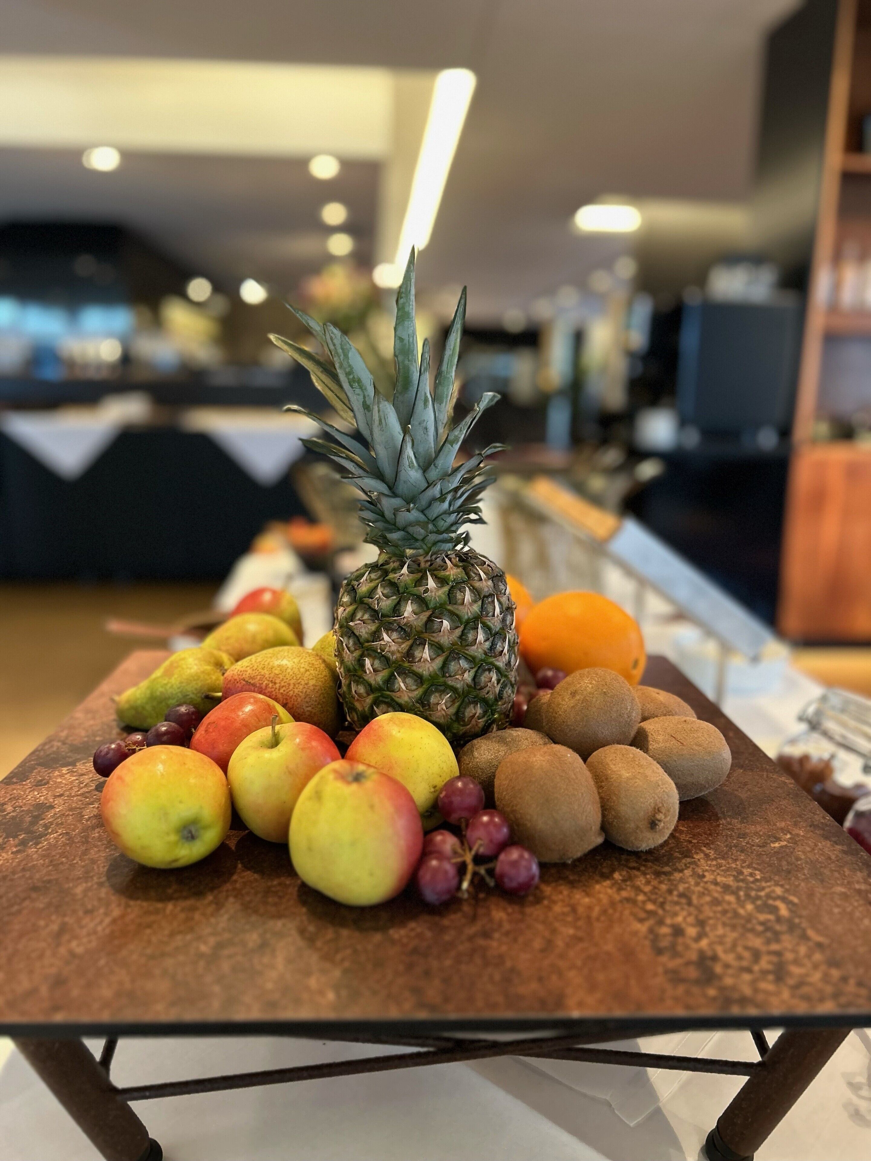 A fruit display with a pineapple, apples, grapes, and kiwis on a table in a hotel lobby.