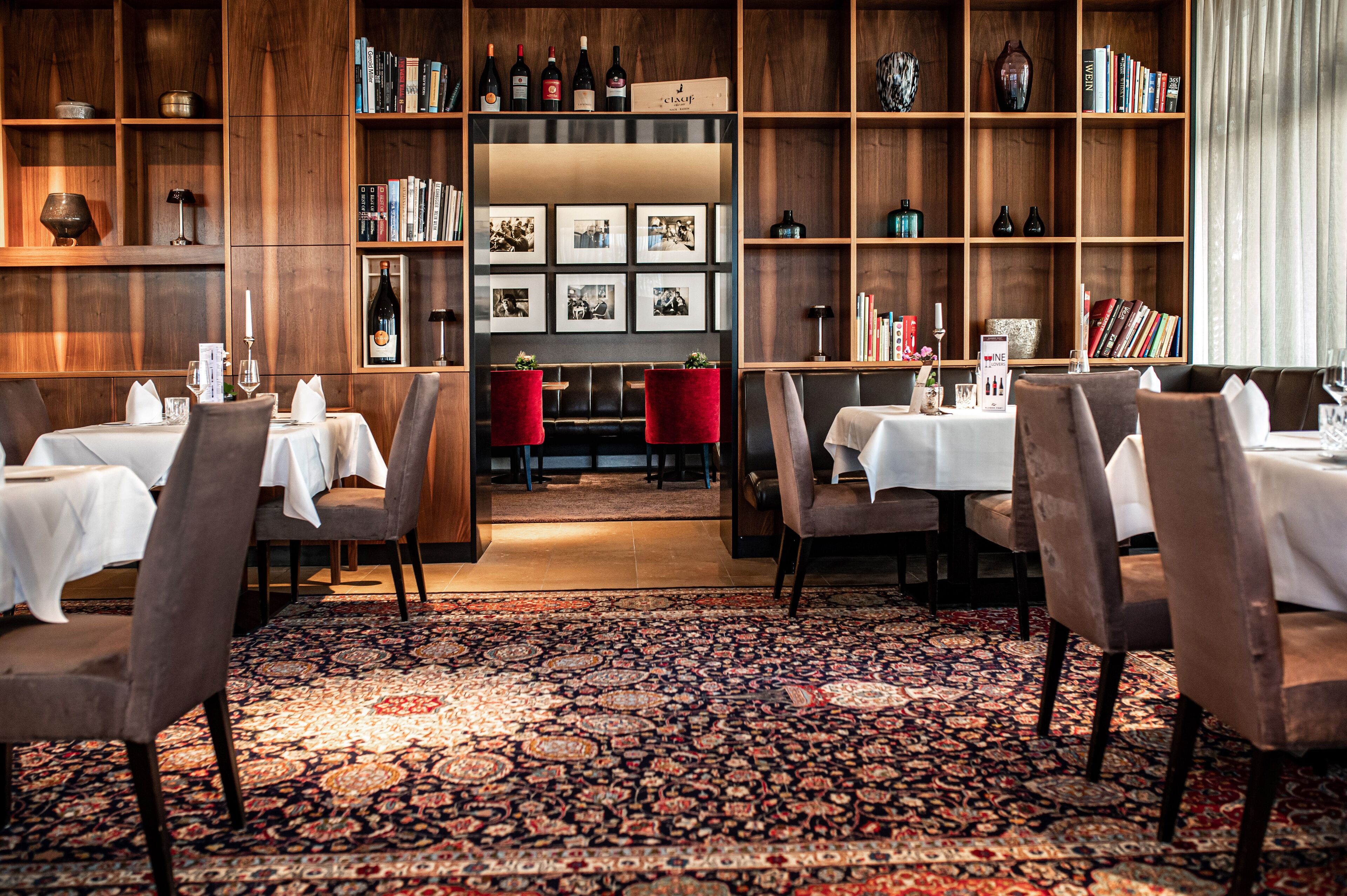 Un restaurante con estanterías de madera, mesas con manteles blancos y una alfombra estampada.