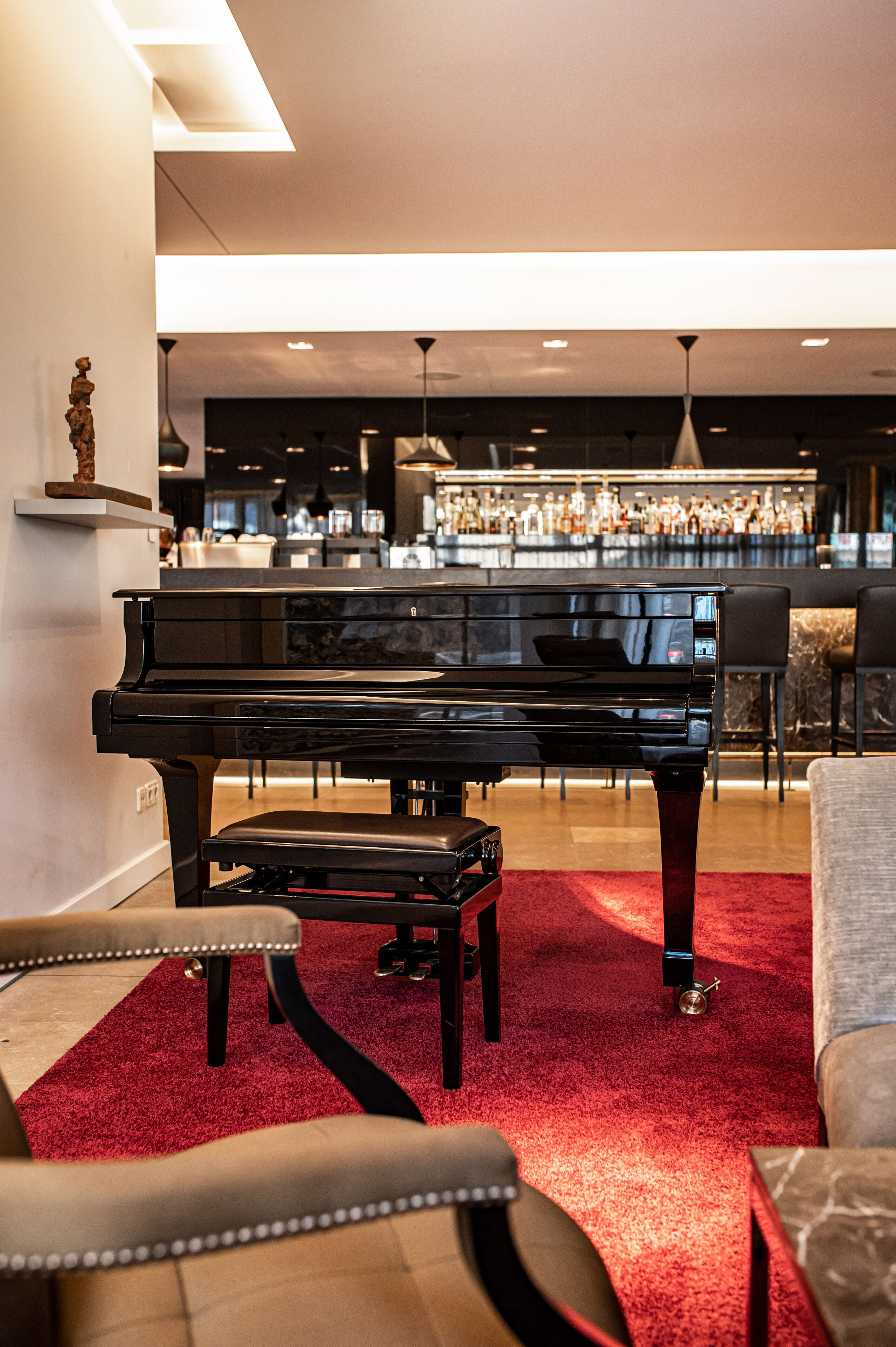Un piano de cola en una sala de estar con alfombra roja, un área de bar al fondo y muebles modernos.