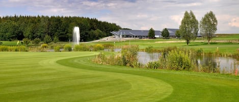 A golf course with a pond, trees, and a building in the background.