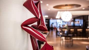 A modern interior with a red abstract sculpture on a wall, a bar area in the background, and a chandelier.