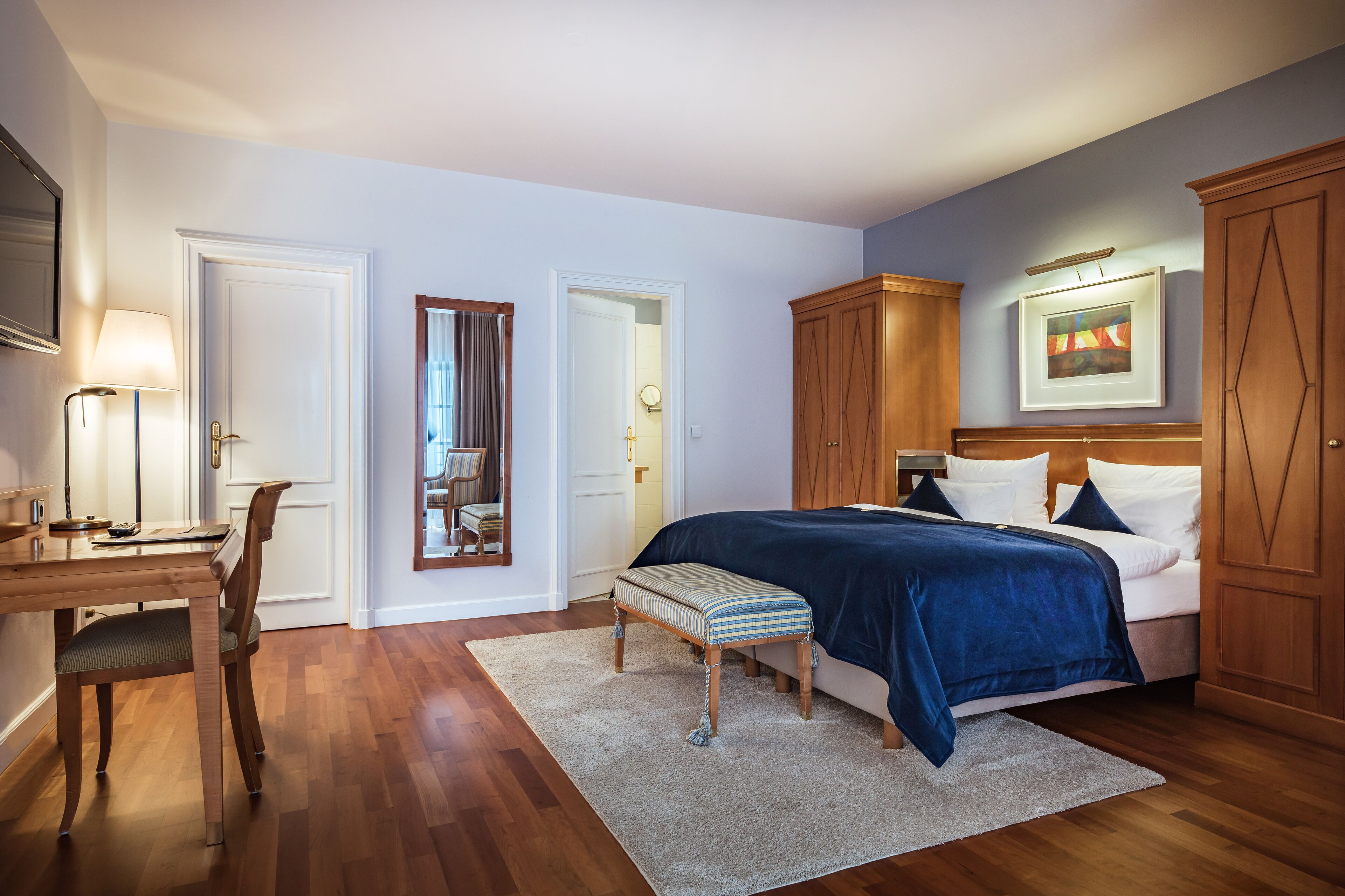 A bedroom with a bed, bedside table, lamp, chair, and a door leading to another room.