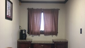 A small, compact room with a kitchenette, a single chair, a trash bin, and a framed picture on the wall. - Budget Inn Clearfield (Clearfield)