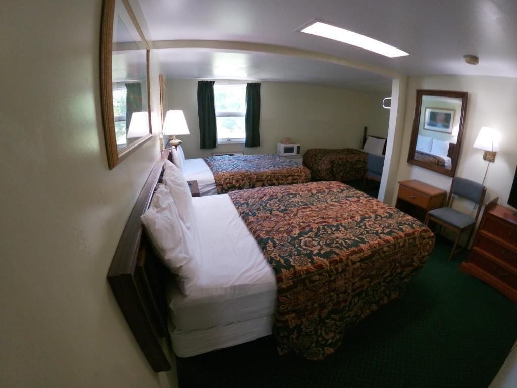 A hotel room with two beds, a desk, a chair, a mirror, and a window.