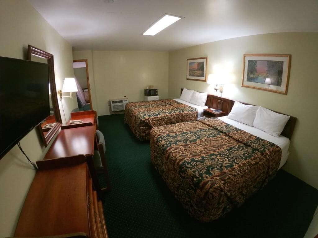 A hotel room with two beds, a desk, a television, and a painting on the wall.