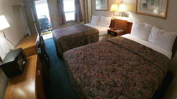 Quarto de hotel com duas camas, uma mesa, uma cadeira, uma televisão e uma janela com cortinas.