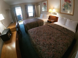 Habitación de hotel con dos camas, un escritorio, una silla, un televisor y una ventana con cortinas.