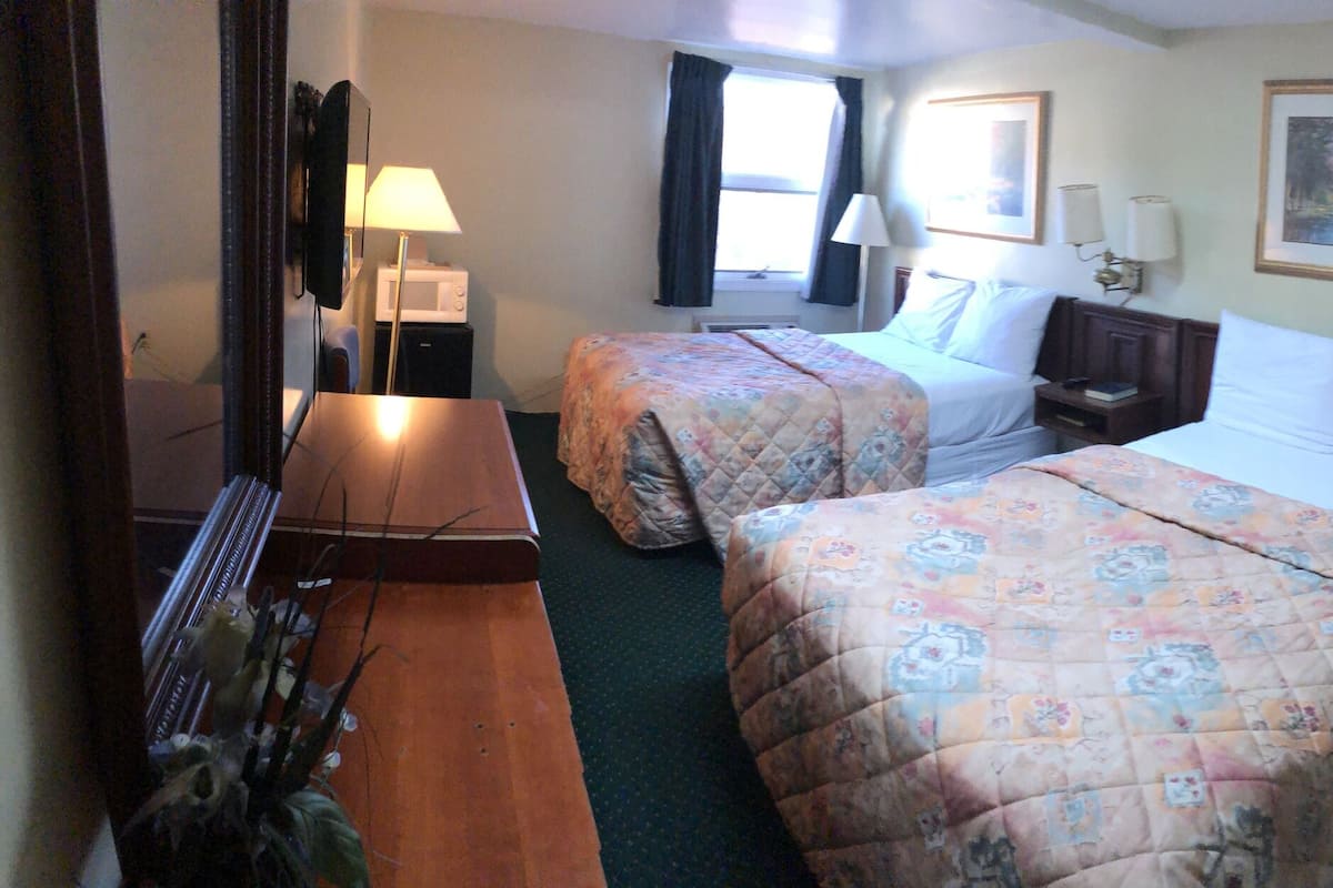 A hotel room with two beds, a desk, a chair, a bathroom with a toilet and bathtub, and a window with curtains.