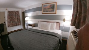 A hotel room with a bed, a nightstand, a lamp, a painting, and a radiator. - Budget Inn Clearfield (Clearfield)