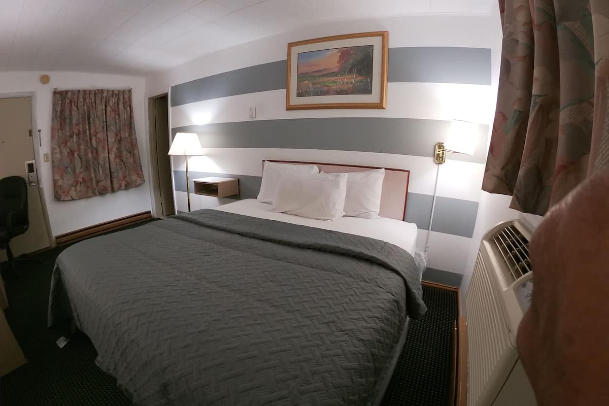 A hotel room with a bed, a nightstand, a lamp, a painting, and a radiator.