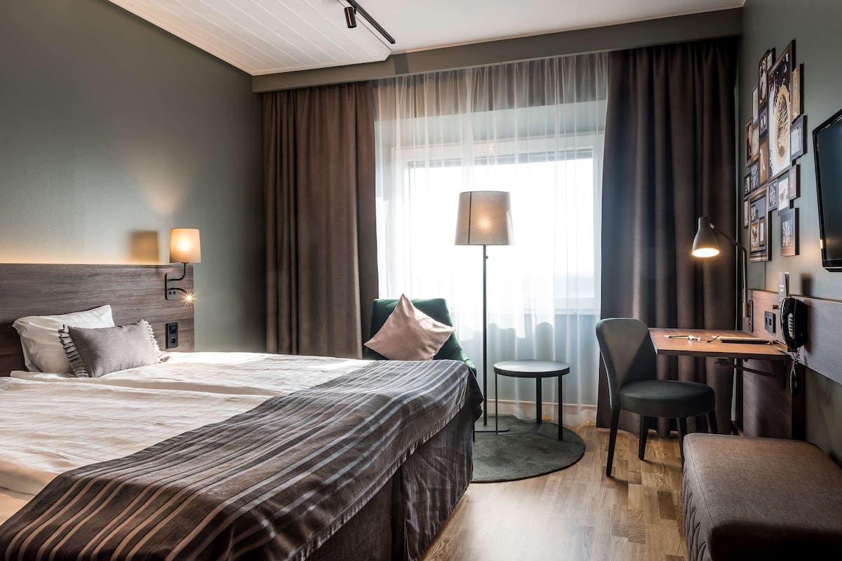 Une chambre d’hôtel avec un grand lit, un bureau avec une chaise, une petite table et une lampe.