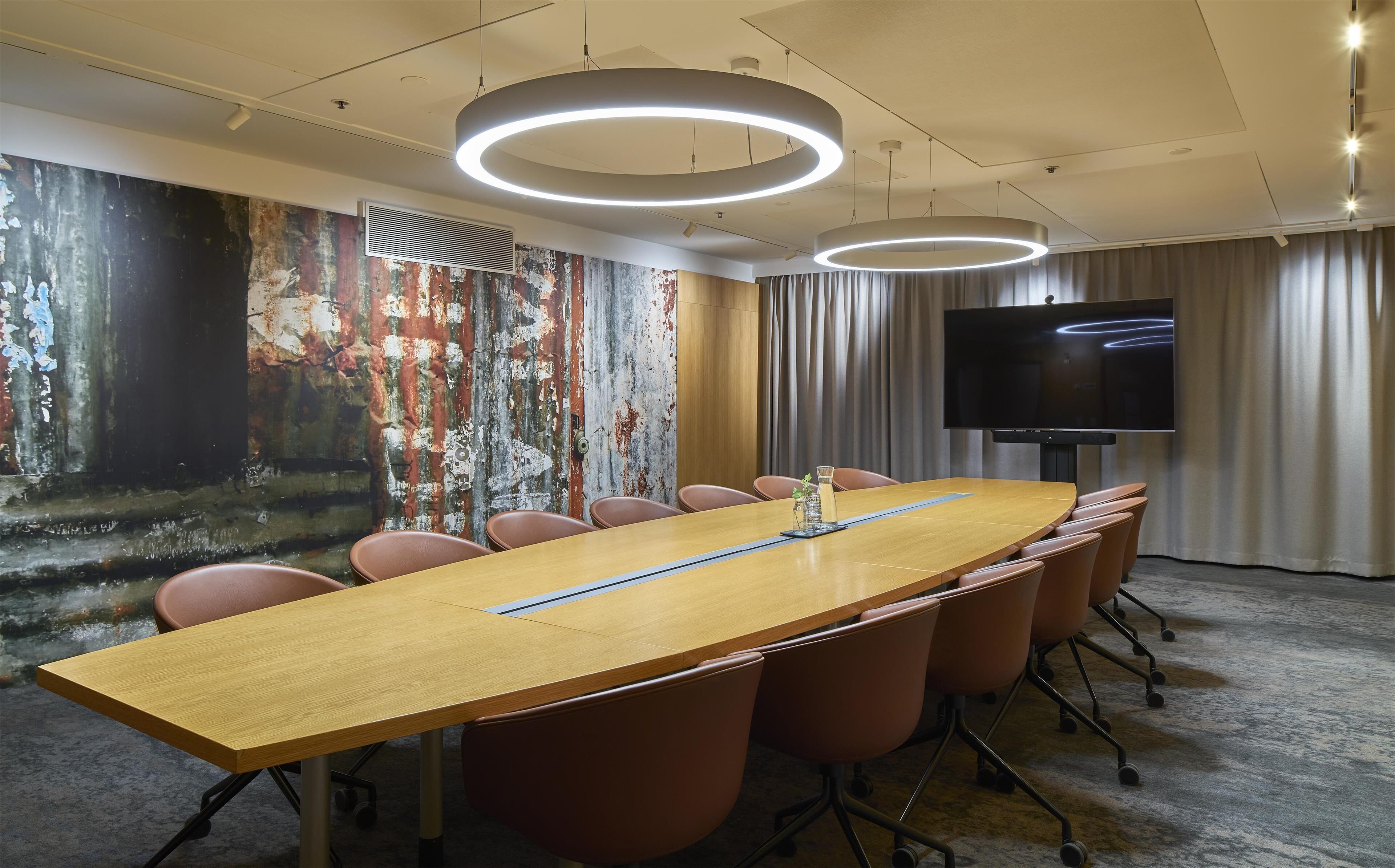 A conference room with a long table, chairs, a flat-screen TV, and a mural on the wall.