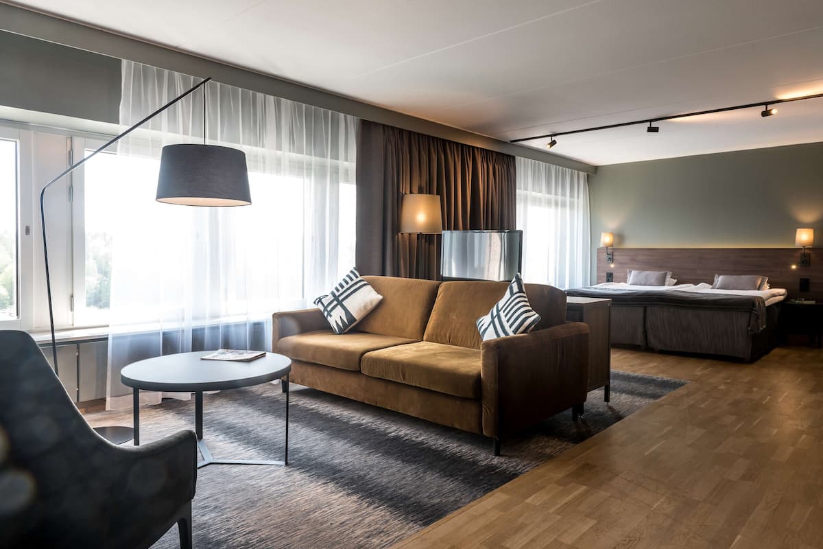 Une chambre d’hôtel moderne avec un canapé, une petite table, une lampe et un lit.
