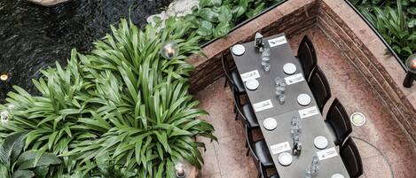 A dining area with a table set for four, surrounded by lush green plants and a stone wall.