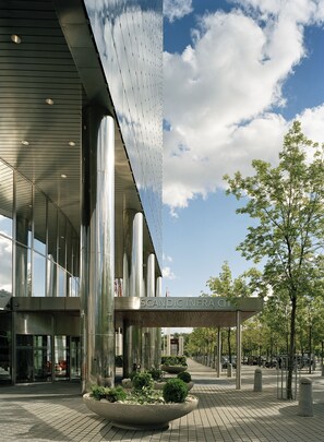 A modern building with a glass facade, large planters with greenery, and a clear sky. - Scandic Infra City (Upplands Vasby)