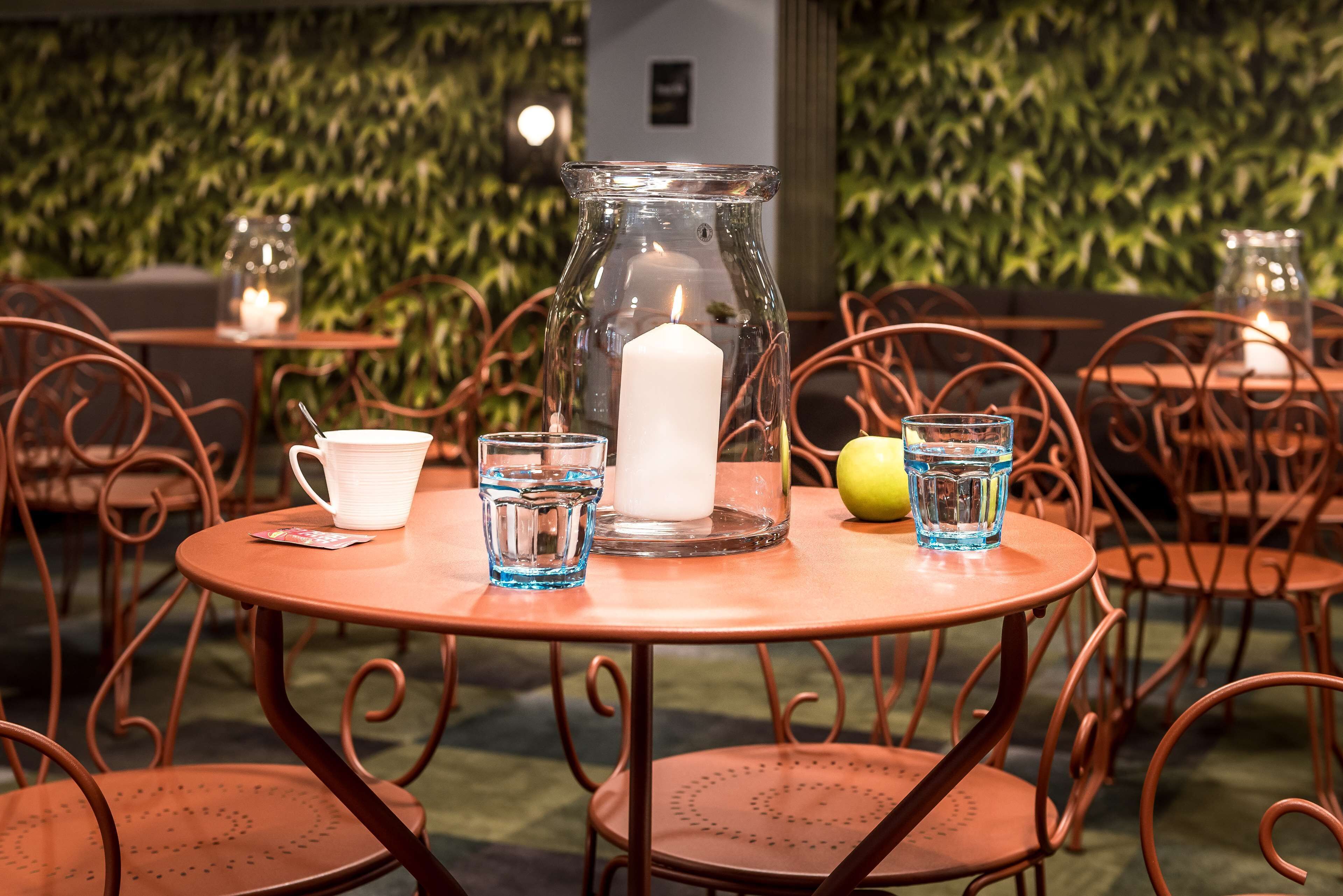 Una mesa redonda con una jarrón de vidrio, una vela blanca, un vaso de agua y un limón.
