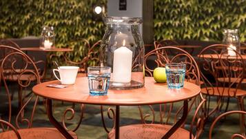 Una mesa redonda con una jarrón de vidrio, una vela blanca, un vaso de agua y un limón.