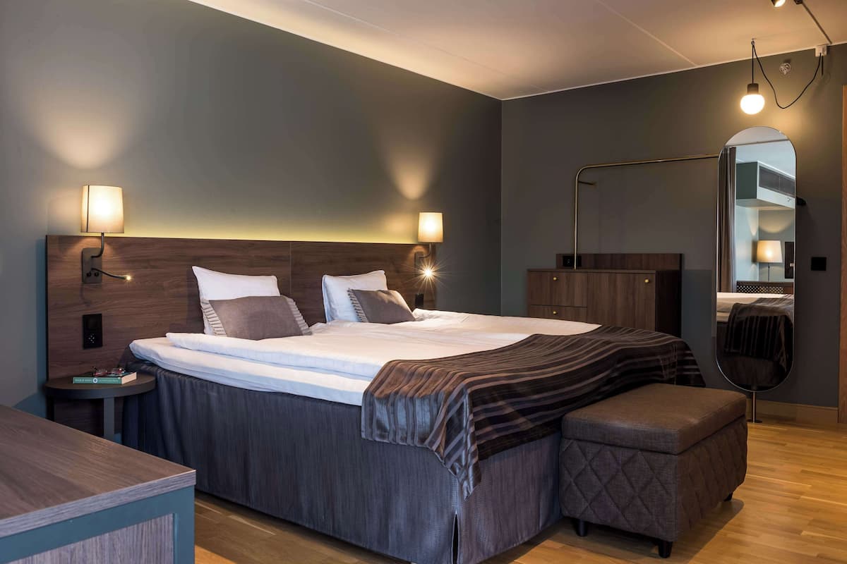 Une chambre d’hôtel moderne avec un grand lit, des tables de chevet, un miroir et un petit coin salon.