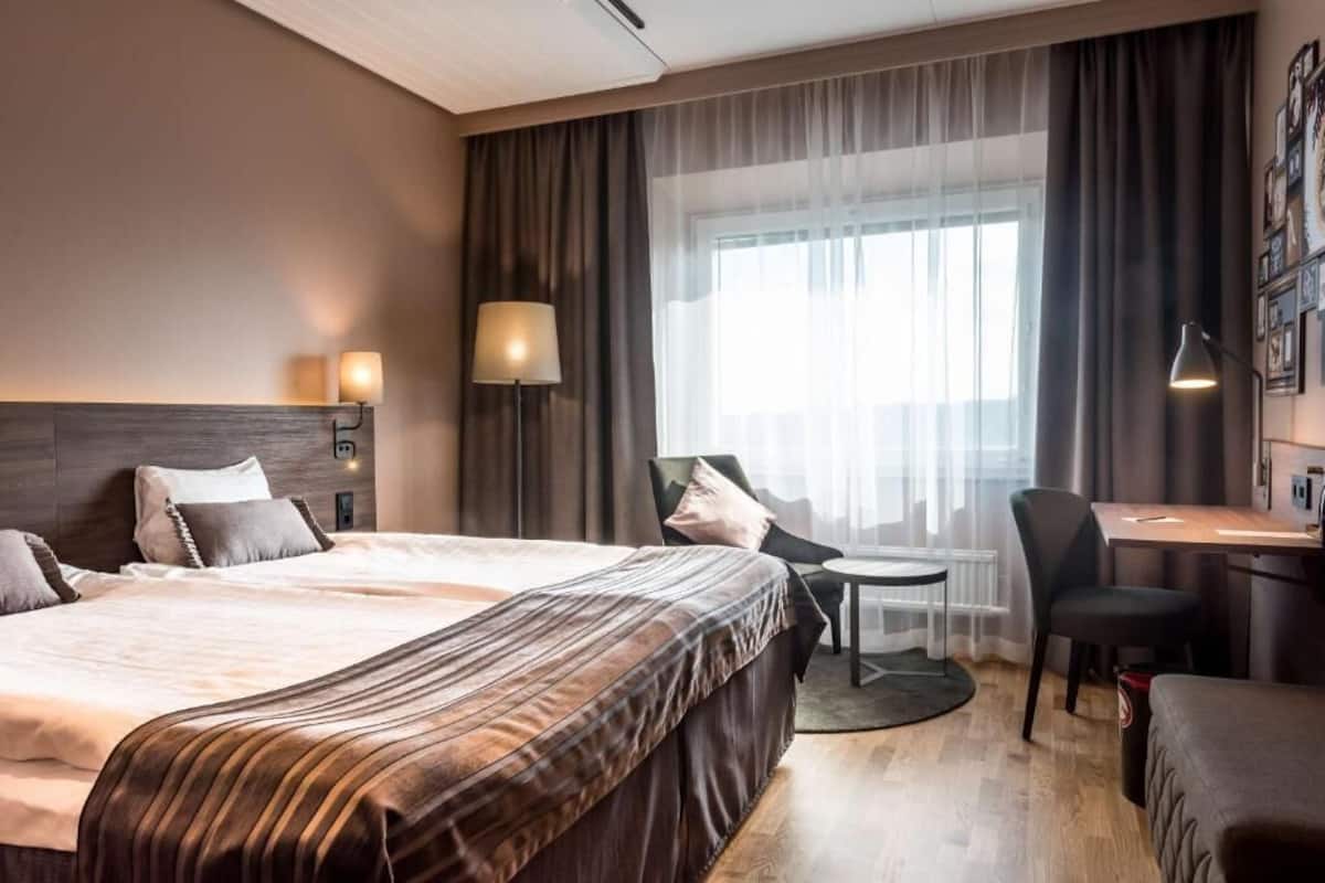 A hotel room with a large bed, a desk, a chair, and a small table.