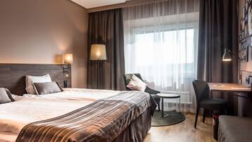 A hotel room with a large bed, a desk, a chair, and a small table.