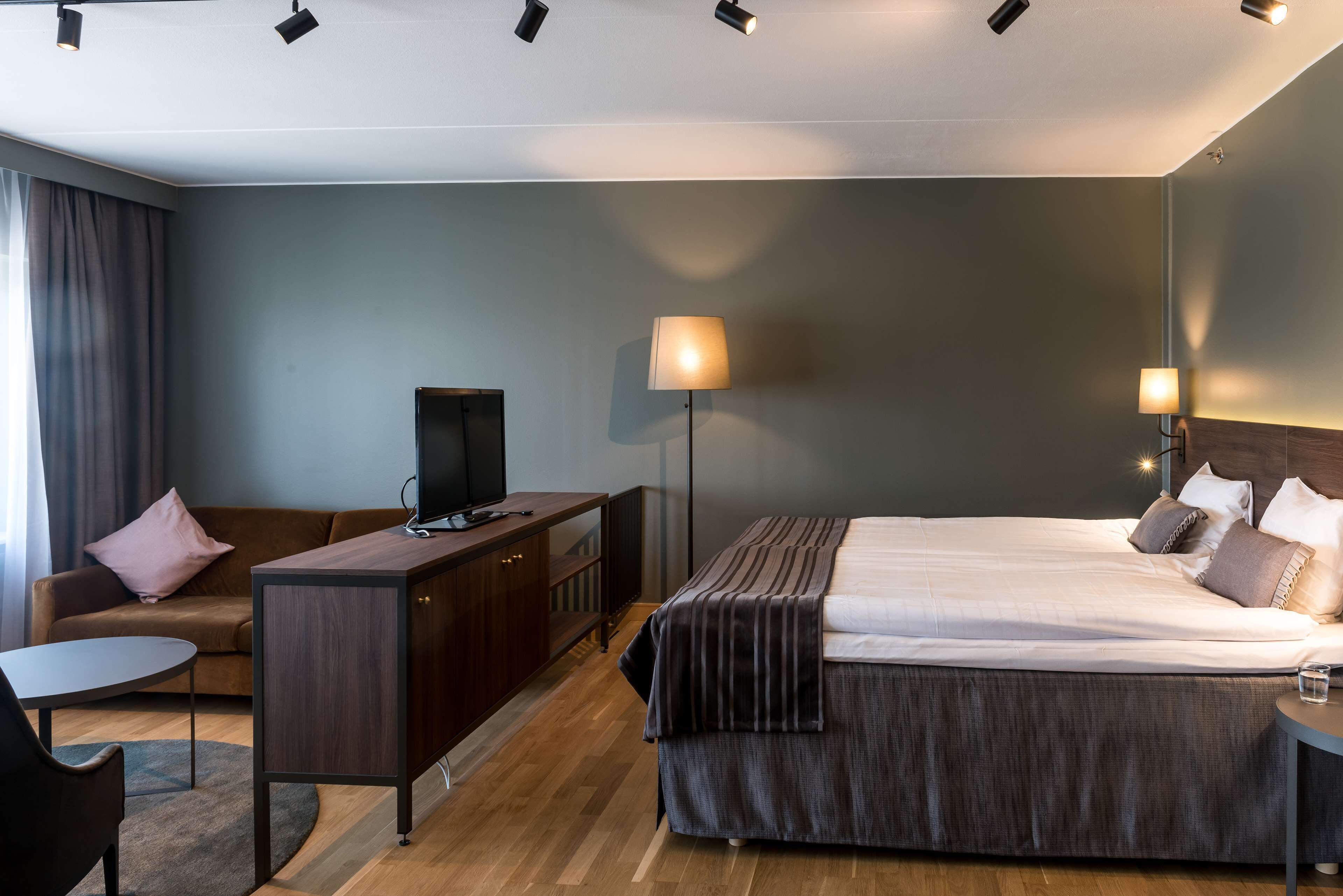 A hotel room with a bed, a desk, a television, and a lamp.