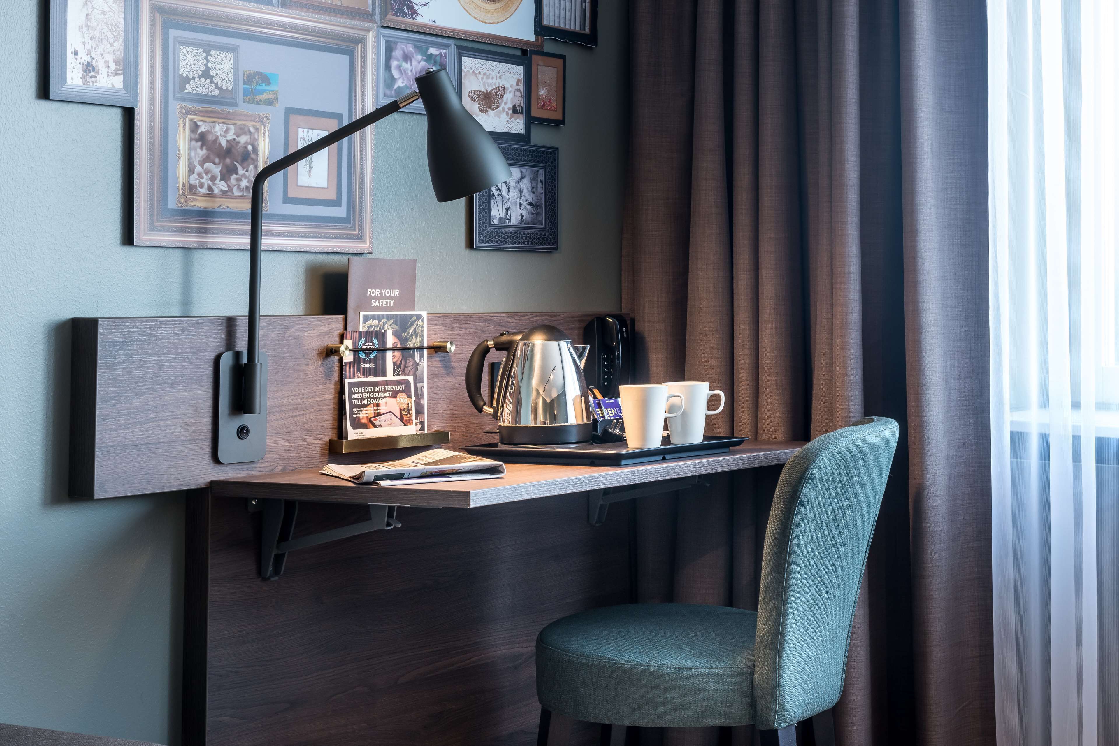 Un espacio de trabajo moderno con escritorio, silla, lámpara, cafetera y cuadros en la pared.