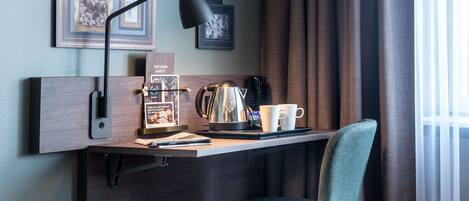 Un espacio de trabajo moderno con escritorio, silla, lámpara, cafetera y cuadros en la pared.