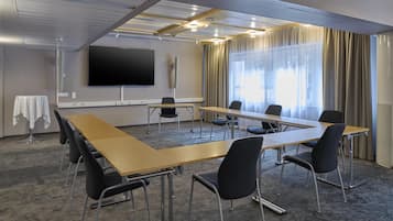 Ett konferensrum med ett långt bord, stolar, en platt-TV och ett stort fönster med gardiner.