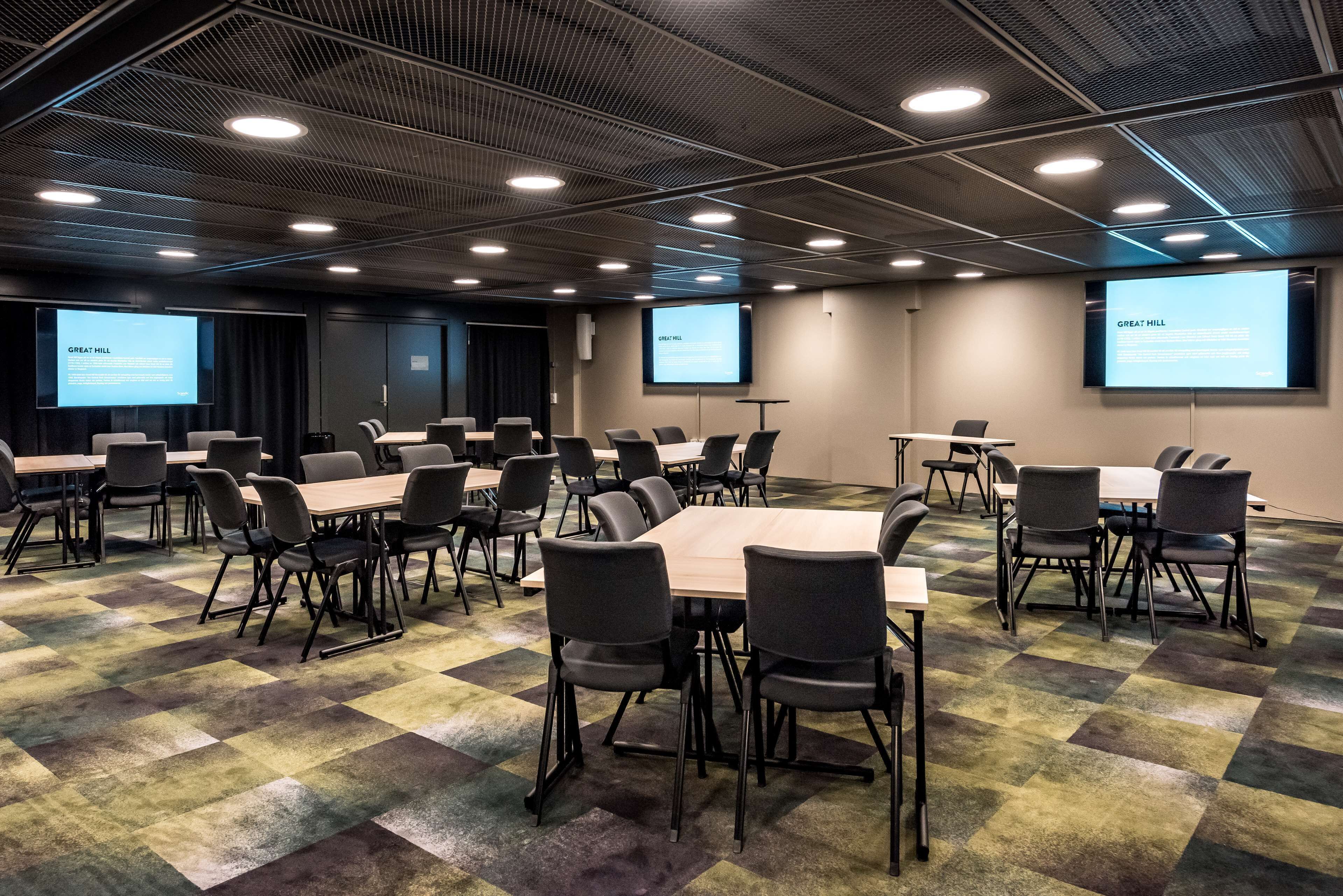 Een congreszaal met meerdere tafels en stoelen, een projectiescherm waarop 'GREAT HILL' staat, en een vloerbedekking.