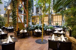 Enjoy a sophisticated dining experience in this elegant space, featuring a variety of seating arrangements and lush greenery.